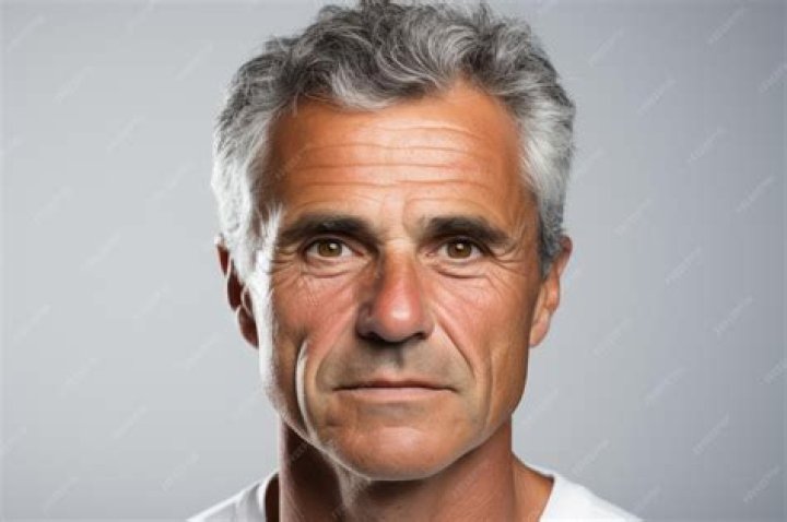 a man with grey hair wearing a black suit and neck tie smiling at the